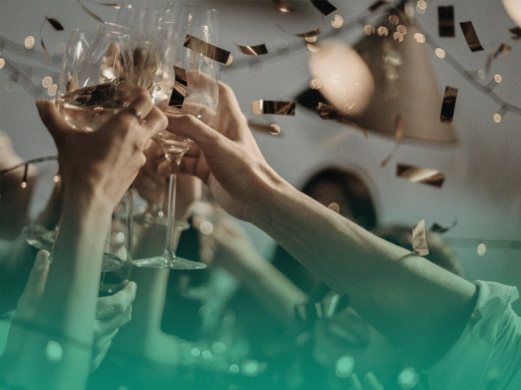 Pessoas brindando com taças de champanhe em uma festa de formatura, com pedaços de papel dourado caindo ao fundo.