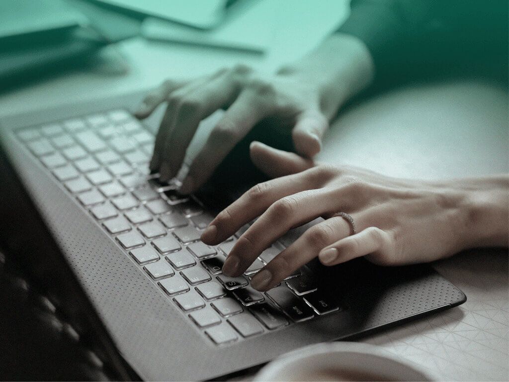 Mulher digitando em um laptop preto, criando seu site de formatura.