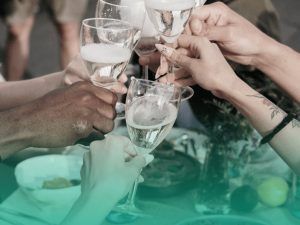 Seis mãos de pessoas brindando com taças de champanhe em uma festa de formatura simples.